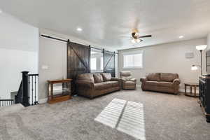 Living room featuring a textured ceiling, a barn door, carpet flooring, and ceiling fan