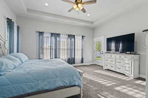 Carpeted bedroom featuring a raised ceiling and ceiling fan