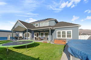 Back of property with ceiling fan, a hot tub, a patio area, a mountain view, and a lawn