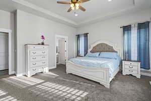 Bedroom featuring ceiling fan, a tray ceiling, and dark colored carpet