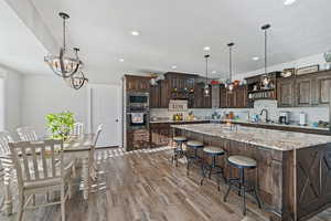 Kitchen with a large island, hardwood / wood-style floors, dark brown cabinets, stainless steel appliances, and decorative light fixtures