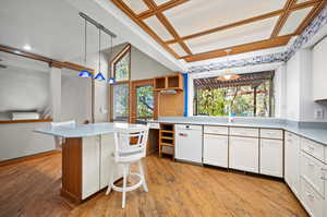 Kitchen featuring white cabinets, a breakfast bar area, light hardwood flooring, dishwasher, and pendant lighting