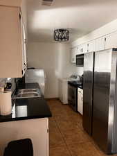 Kitchen featuring washer / dryer, sink, dark tile patterned floors, stainless steel appliances, and white cabinets