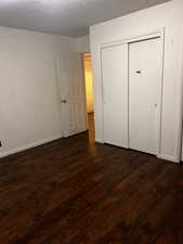 Unfurnished bedroom featuring a closet, dark hardwood / wood-style floors, and a textured ceiling