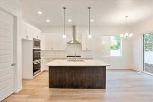 Kitchen with a kitchen island with sink, light hardwood / wood-style floors, wall chimney exhaust hood, and white cabinets