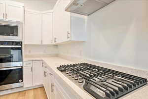 Kitchen featuring light hardwood / wood-style floors, white cabinets, light stone countertops, and stainless steel appliances