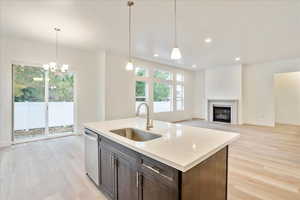 Kitchen with a kitchen island with sink, dishwasher, light hardwood / wood-style floors, decorative light fixtures, and sink