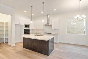 Kitchen featuring sink, wall chimney range hood, appliances with stainless steel finishes, and white cabinetry