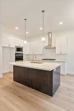 Kitchen featuring wall chimney range hood, decorative light fixtures, stainless steel appliances, and sink