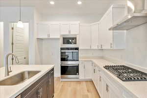 Kitchen featuring sink, white cabinetry, and wall chimney range hood