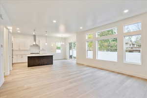 Kitchen with a healthy amount of sunlight, wall chimney range hood, decorative light fixtures, and a center island with sink