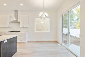 Kitchen featuring white cabinets, an inviting chandelier, pendant lighting, light hardwood / wood-style floors, and wall chimney exhaust hood