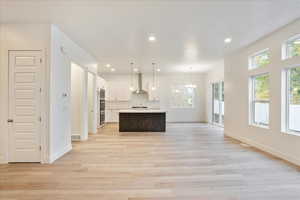 Kitchen with a center island with sink, white cabinetry, light hardwood / wood-style flooring, wall chimney exhaust hood, and decorative light fixtures