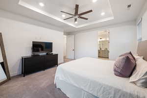 Carpeted bedroom featuring ceiling fan, ensuite bathroom, and a raised ceiling