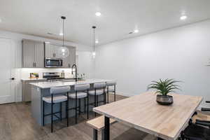 Kitchen with hanging light fixtures, dark hardwood / wood-style flooring, appliances with stainless steel finishes, a kitchen island with sink, and gray cabinetry