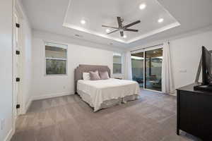 Carpeted bedroom with ceiling fan, a raised ceiling, and access to exterior