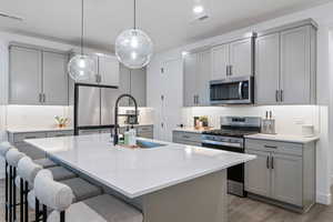 Kitchen with hanging light fixtures, dark hardwood / wood-style flooring, appliances with stainless steel finishes, an island with sink, and sink