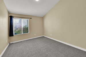 Carpeted empty room featuring vaulted ceiling