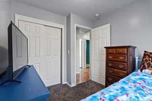 Bedroom with dark carpet, a textured ceiling, and a closet