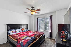 Bedroom featuring a textured ceiling, dark carpet, and ceiling fan