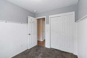 Unfurnished bedroom featuring dark colored carpet, a textured ceiling, and a closet