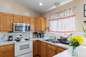 Kitchen with decorative backsplash, white electric range oven, sink, and vaulted ceiling