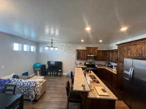 Kitchen with a center island with sink, appliances with stainless steel finishes, light stone countertops, dark wood-type flooring, and dark brown cabinetry