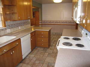 Kitchen with kitchen peninsula, decorative backsplash, sink, and white appliances