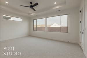 Carpeted spare room featuring ceiling fan and a tray ceiling