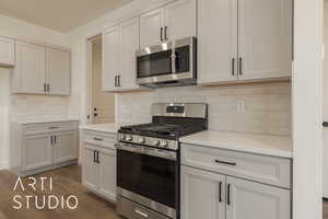 Kitchen with stainless steel appliances, dark hardwood / wood-style floors, decorative backsplash, and white cabinets