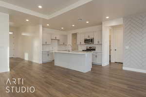 Kitchen featuring appliances with stainless steel finishes, an island with sink, white cabinets, dark hardwood / wood-style flooring, and decorative backsplash