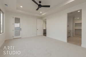 Unfurnished bedroom featuring ceiling fan, ensuite bathroom, light carpet, a walk in closet, and a raised ceiling