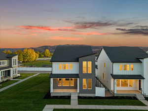 Back house at dusk featuring a mountain view and a lawn