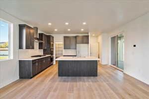 Kitchen featuring appliances with stainless steel finishes, sink, wall chimney exhaust hood, light hardwood / wood-style flooring, and a kitchen island with sink