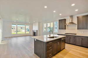 Kitchen featuring wall chimney range hood, light hardwood / wood-style flooring, a healthy amount of sunlight, and sink