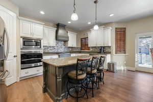 Kitchen with pendant lighting, premium range hood, appliances with stainless steel finishes, a kitchen island, and white cabinetry