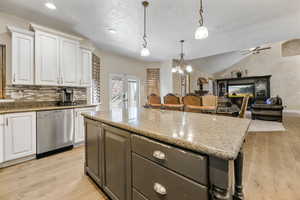 Kitchen with dishwasher, white cabinets, hanging light fixtures, light hardwood / wood-style flooring, and vaulted ceiling