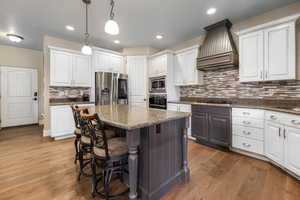 Kitchen featuring stainless steel appliances, pendant lighting, white cabinets, custom exhaust hood, and hardwood / wood-style flooring