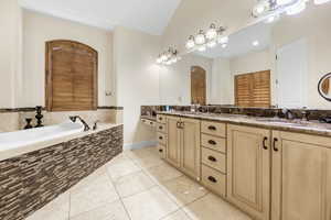 Bathroom with vanity, vaulted ceiling, tiled bath, and tile patterned floors