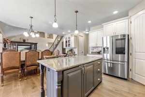 Kitchen with stainless steel fridge, light hardwood / wood-style floors, white cabinetry, and pendant lighting