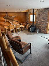 Carpeted living room with log walls, a textured ceiling, and a wood stove