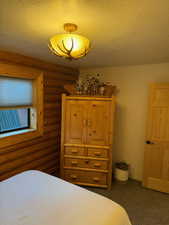 Bedroom with dark colored carpet, rustic walls, and a textured ceiling