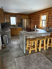 Kitchen with sink, black electric cooktop, stainless steel fridge, log walls, and a breakfast bar area