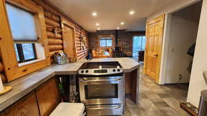 Kitchen with tile countertops, rustic walls, plenty of natural light, stainless steel range, and a wood stove