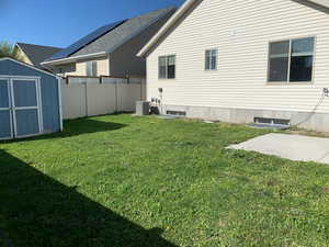 Rear view of house featuring a storage unit, a lawn, and cooling unit