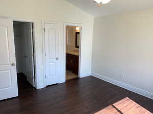 Unfurnished bedroom featuring connected bathroom, lofted ceiling, and dark hardwood / wood-style flooring