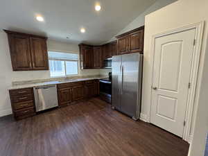 Kitchen with dark hardwood / wood-style floors, sink, vaulted ceiling, appliances with stainless steel finishes, and light stone counters