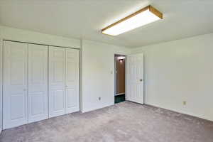 Unfurnished bedroom with light carpet, a closet, and a textured ceiling