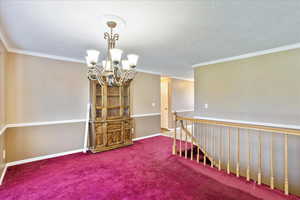 Empty room featuring crown molding, carpet flooring, a textured ceiling, and a chandelier