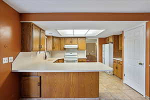 Kitchen featuring sink, kitchen peninsula, white appliances, and light tile patterned floors